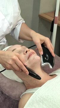Beautician performs a microcurrent facial treatment on a mature woman in a beauty salon, anti aging skincare, lifting, rejuvenation, professional care.
