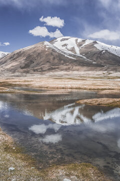 Clear-water rivers and lakes in a mountain valley, pastures and green grassy fields set against mountain ranges and snow-capped, glacier-clad peaks&mdash;a scenic landscape background