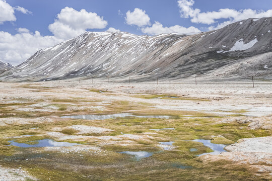 Clear-water rivers and lakes in a mountain valley, pastures and green grassy fields set against mountain ranges and snow-capped, glacier-clad peaks&mdash;a scenic landscape background