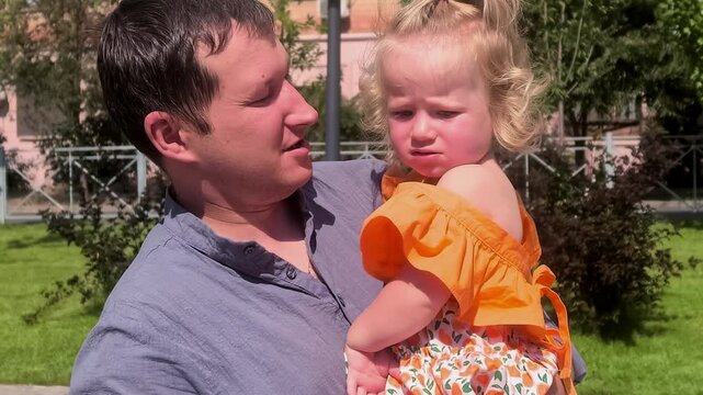 Father comforts his upset toddler daughter outdoors, parental support, emotional care, family bonding, childhood reassurance, loving relationship.