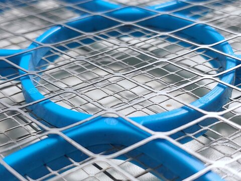 Close-up of an electric mosquito swatter racket, highlighting the intricate geometric patterns of its layered metal grid and blue plastic frame