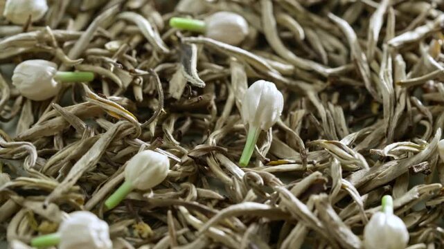 Macro video of white jasmine flowers and fresh buds mixed with dried silver needle tea leaves, traditional chinese tea scenting process and organic herbal beverage culture background