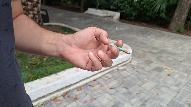 Close-up of a man's hand holding a cigarette outdoors in a park