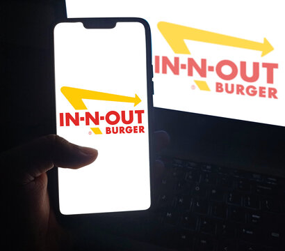In-N-Out Burger logo displayed on smartphone with matching logo on laptop screen illustrative editorial