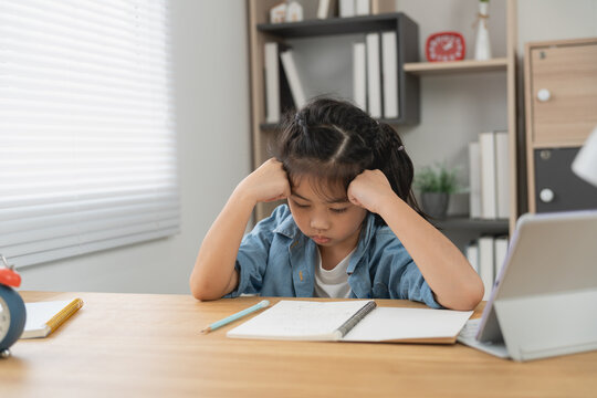 Young girl sitting at wooden desk with notebook and pencil frustrated struggling with homework study at home