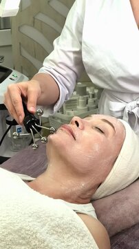 Beautician performs a microcurrent facial lifting procedure on a mature female client, anti aging skincare, toning, rejuvenation, professional beauty care.