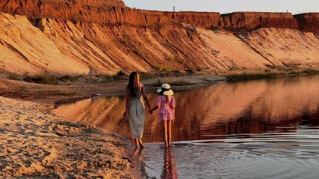 Mother and daughter walk hand in hand into a lake at sunset, family bonding, summer adventure, maternal love, peaceful outdoor lifestyle.