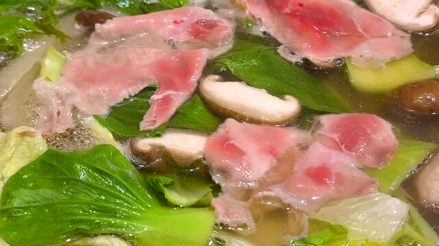 japanese shabu shabu hot pot with pork slices, vegetables and mushroom simmering in broth on a table during winter dinner