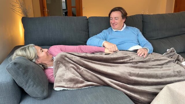 Slow motion video of romantic middle-aged couple relaxing on a couch, holding hands, and talking affectionately at home