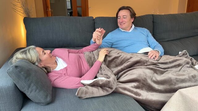Senior couple holding hands and chatting affectionately while relaxing together on a cozy couch