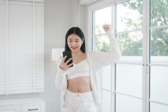 Smiling young woman in white clothes talking on a phone by a bright window at home, creating a calm, fresh, and modern lifestyle scene with natural light.