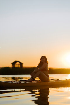 Woman resting on a paddle board at golden sunset