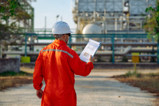 Industrial engineer reviewing inspection report while monitoring refinery operations. Engineering documentation, preventive maintenance, equipment assessment, safety compliance and plant management.