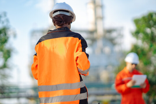 Industrial engineer viewed from behind conducting refinery inspection with engineering documents. Field operations, maintenance planning, industrial infrastructure and technical evaluation.