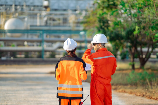 Maintenance engineers reviewing refinery operations during outdoor site inspection. Engineering teamwork, equipment monitoring, operational planning and industrial infrastructure management.
