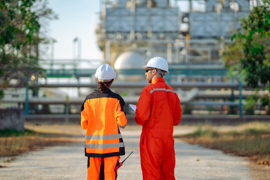 Industrial engineers walking through refinery site while inspecting maintenance documents and plant conditions. Engineering collaboration, preventive maintenance, safety inspection operations.