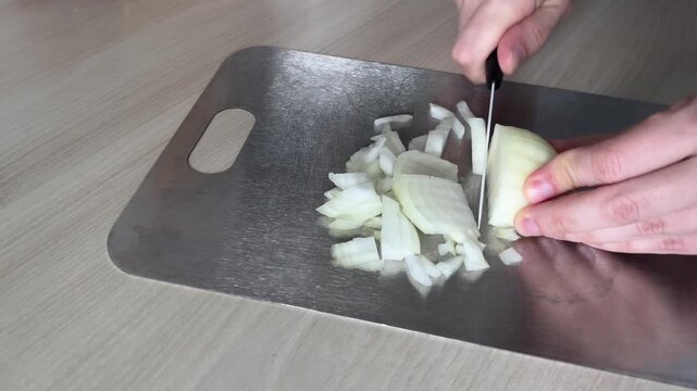 Woman hands chopping fresh onions with a knife on a metal board, ingredient preparation for homemade dinner