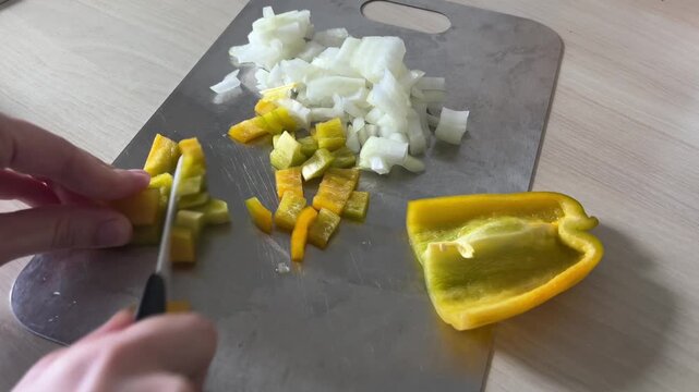 Woman slicing fresh bell peppers on a stainless steel cutting board in a bright home kitchen, healthy food prep