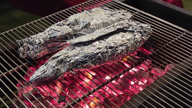 charcoal grilled fish wrapped in aluminum foil cooking over open fire during outdoor bbq, smoky and juicy summer meal