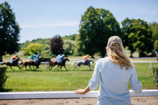 Woman spectator is watching and enjoying horse racing on sunny day at racetrack