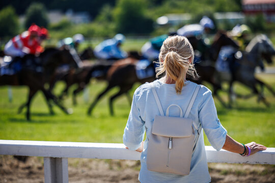 Woman spectator watching running racehorses during horse racing event