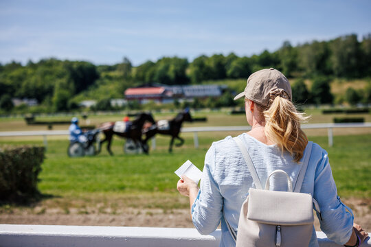 Woman holding betting slip during trotting race. Bettor or gambler watching harness racing after placing bet at racecourse