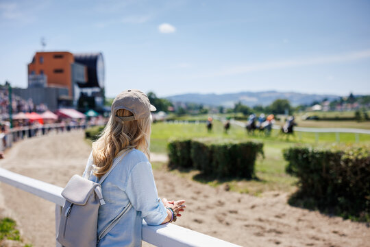 Woman spectator watching horse racing at sunny racecourse