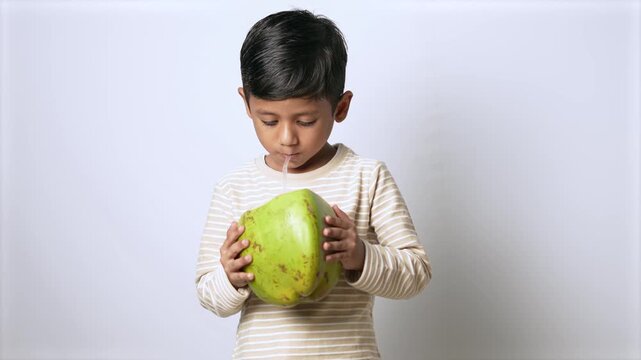Indian boy drinking fresh coconut water. Child enjoying healthy tropical fruit beverage.