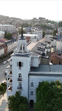 Aerial drone footage orbiting an ornate clock tower and historic building in the old town of telavi, georgia, revealing the cityscape and alazani valley in the background