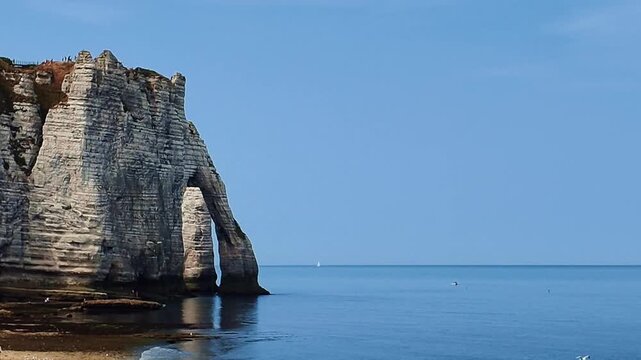 Dramatic white chalk cliffs and natural sea arch rise above the blue waters of the English Channel at Etretat, Normandy