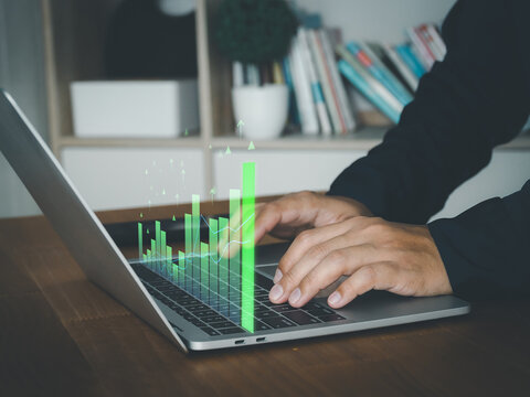 Laptop computer with business graph on screen, hands typing on keyboard in office interior, data analysis and finance concept, focused work
