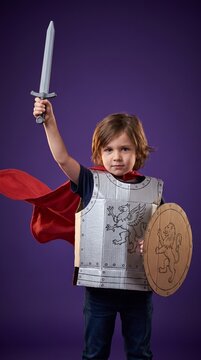 Brave Little Boy in DIY Cardboard Knight Armor Holding Toy Sword and Shield, Heroic Portrait on Purple Background