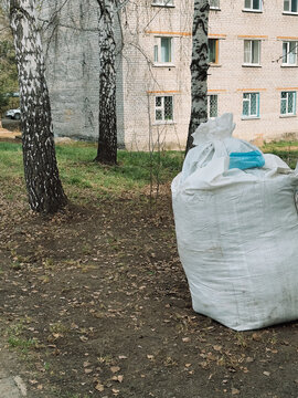 Large white bag with fallen leaves and yard waste after outdoor cleanup near apartment building.