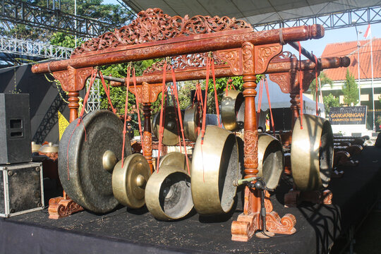 Yogyakarta - Indonesia, June 19, 2024 Traditional gong set hangs beneath carved wooden frame. Gongs vary in size, gleam with age and use. Carved frame rests on dark cloth under tent. Cultural instrume