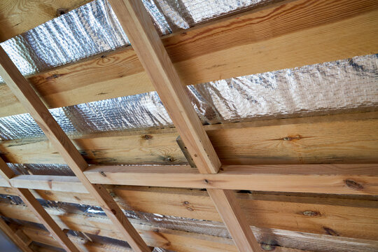 Wooden roof framing with installed silver radiant barrier foil insulation attached to timber rafters inside residential building attic under construction.