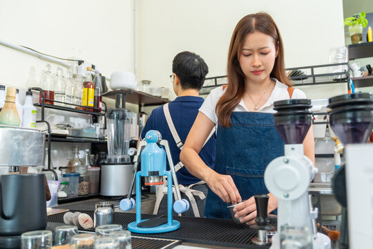 Small business entrepreneur coffee shop cafe restaurant. Asian woman barista using manual espresso maker making freshly brewed coffee on bar counter. Waitress serving beverage drink to customer.