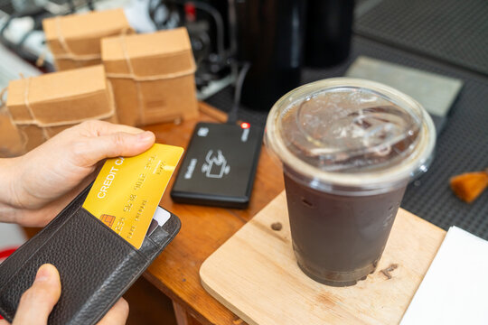 Credit card payment at coffee shop counter. Cafe owner using card reader for cashless transaction while serving coffee drink to customer. Electronic payment technology for small business retail store.