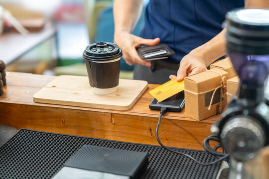 Credit card payment at coffee shop counter. Cafe owner using card reader for cashless transaction while serving coffee drink to customer. Electronic payment technology for small business retail store.