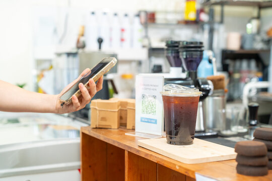 Cashless qr code payment by smartphone at coffee shop, customer scanning mobile payment electronic banking while cafe owner serving takeaway coffee, digital transaction and small business technology