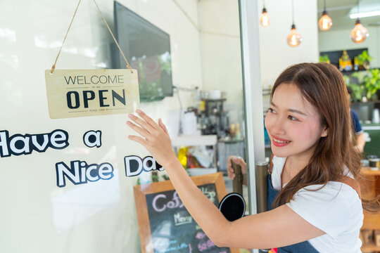 Small business owner opening coffee shop and hanging open sign on glass door, smiling young cafe worker welcoming customers at local cafe, entrepreneurship and retail business concept