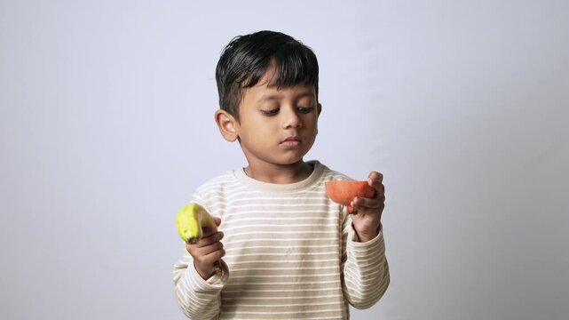 Indian boy choosing between healthy fruits. Child deciding between fresh banana and orange.