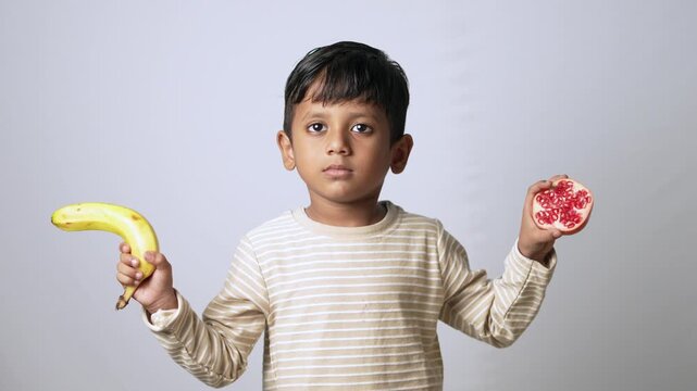Indian boy holding banana and pomegranate. Child choosing healthy fresh organic fruit snacks.