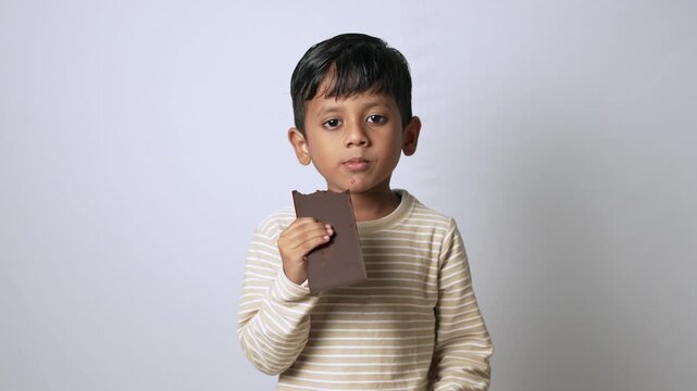 Indian boy eating chocolate bar. Happy child enjoying sweet snack with ok hand gesture.