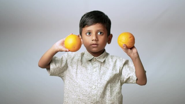 Indian boy holding fresh oranges. Child choosing healthy fruit for a balanced diet.