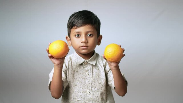 Indian boy holding fresh oranges. Healthy child with citrus fruit for nutrition concept.