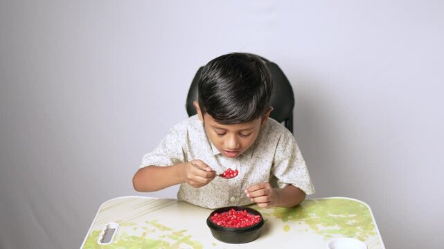 Indian boy eating pomegranate seeds. Child having healthy fruit snack at home.