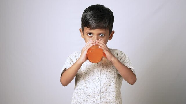 Indian boy drinking orange juice. Child enjoying a healthy fruit beverage in studio.