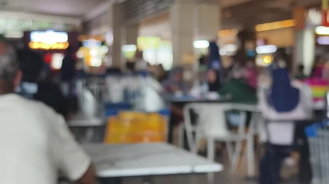 Intentionally blurred footage of customers dining at tables inside a busy shopping mall food court.