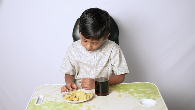 Indian boy eating snacks and drinking soda. Child having lunch at home in Delhi NCR.