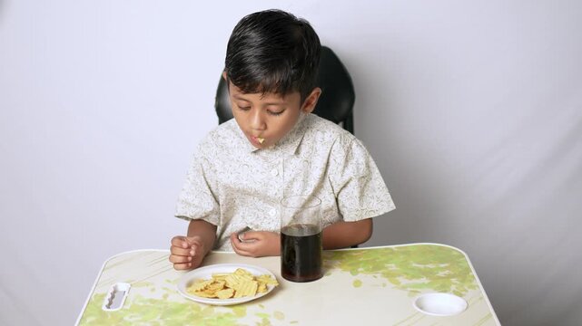 Indian boy eating snacks at home. Child having crispy crackers and soda in Delhi NCR.